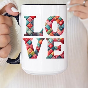 May include: White ceramic mug with a black rim and handle. The mug features the word "LOVE" in large, colorful letters made up of a patchwork quilt pattern.
