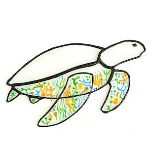 May include: A stained glass sea turtle. The turtle has a white shell and a body decorated with colourful aquatic designs. The outline is black, and the body features green, blue, and orange sea life patterns.