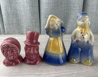May include: A set of four ceramic figurines including a maroon head with a bonnet, a maroon head with a top hat, a figure in a blue dress with a yellow apron and head covering, and a figure in a blue outfit with a yellow scarf and hat.