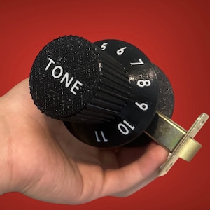 Peut inclure: Un bouton noir avec le mot "TONE" imprimé dessus. Le bouton est relié à un cadran noir avec des chiffres blancs de 5 à 11.