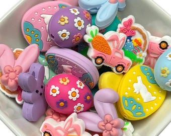 May include: A collection of colorful Easter-themed silicone charms featuring bunnies, eggs, and a truck with the text "Happy Easter".