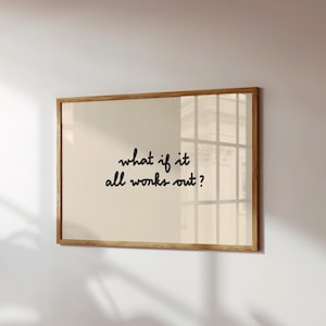 May include: A framed print with the text "what if it all works out?" in a handwritten style. The frame is made of light brown wood, and the background is a light beige color. The print is hanging on a white wall.