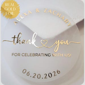 May include: A circular, translucent sticker featuring real gold foil text. The design includes the names Alexa & Zachary, the phrase thank you with a heart icon, the text FOR CELEBRATING WITH US!, and the date 06.20.2026 printed in gold.