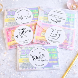 May include: A collection of lottery tickets with personalized stickers. The stickers feature phrases like "Lucky in Love," "Whole lotto love," and "Jackpot!" with names and dates. The tickets are in clear cellophane envelopes.
