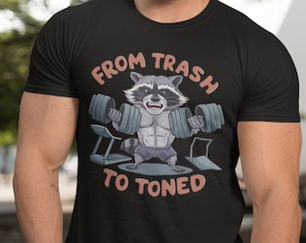 Peut inclure: Un t-shirt noir avec un dessin de raton laveur de bande dessinée soulevant des poids. Le texte sur le t-shirt est "From Trash to Toned".