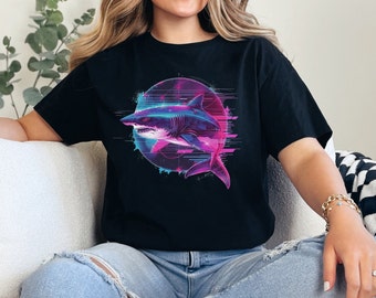 May include: A black t-shirt with a graphic of a shark in a neon pink and blue color scheme. The shark is swimming through a circle with a pixelated background.
