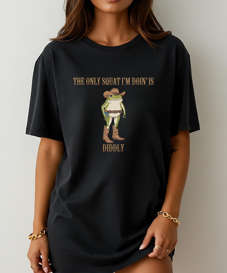May include: Black oversized t-shirt with a graphic of a frog wearing a cowboy hat and boots. The text "The only squat I'm doin' is diddly" is printed on the shirt.