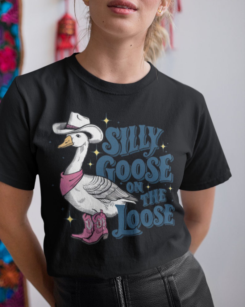 May include: Black t-shirt with a white goose wearing a cowboy hat and pink bandana. The goose is wearing pink cowboy boots. The text "Silly Goose On The Loose" is printed on the shirt in blue.