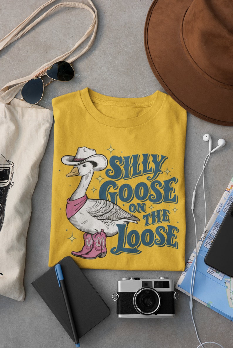 May include: Yellow t-shirt with a cartoon illustration of a goose wearing a cowboy hat and boots. The text "Silly Goose on the Loose" is printed on the shirt.