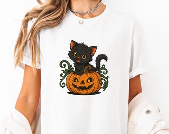 May include: A white t-shirt featuring a black cat perched on a jack-o'-lantern. The cat has a black tail and a white face with yellow eyes. The jack-o'-lantern is orange with a carved face.