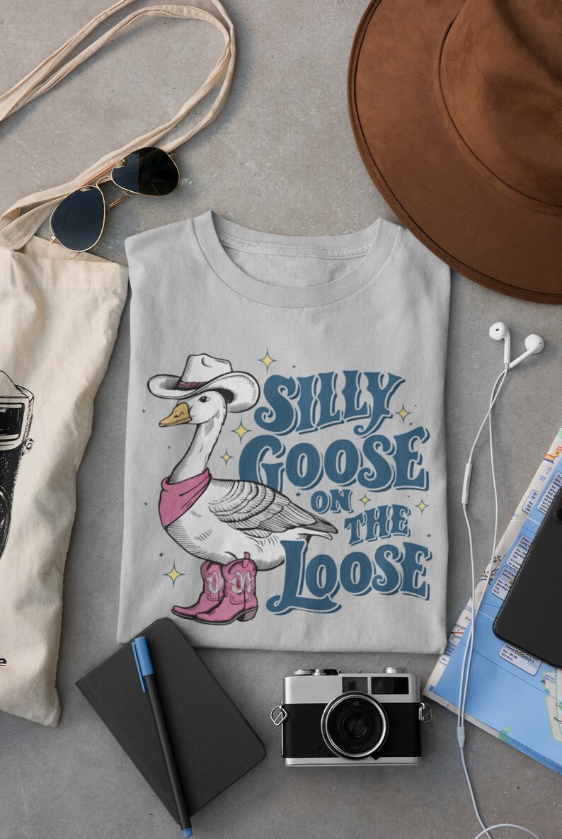 May include: A gray t-shirt with a cartoon goose wearing a cowboy hat and boots. The text "Silly Goose on the Loose" is printed on the shirt.