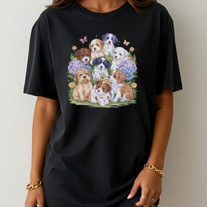 K&ouml;nnte beinhalten: Schwarzes Oversize-T-Shirt mit einem grafischen Druck einer Gruppe von Welpen, umgeben von Blumen und Schmetterlingen.