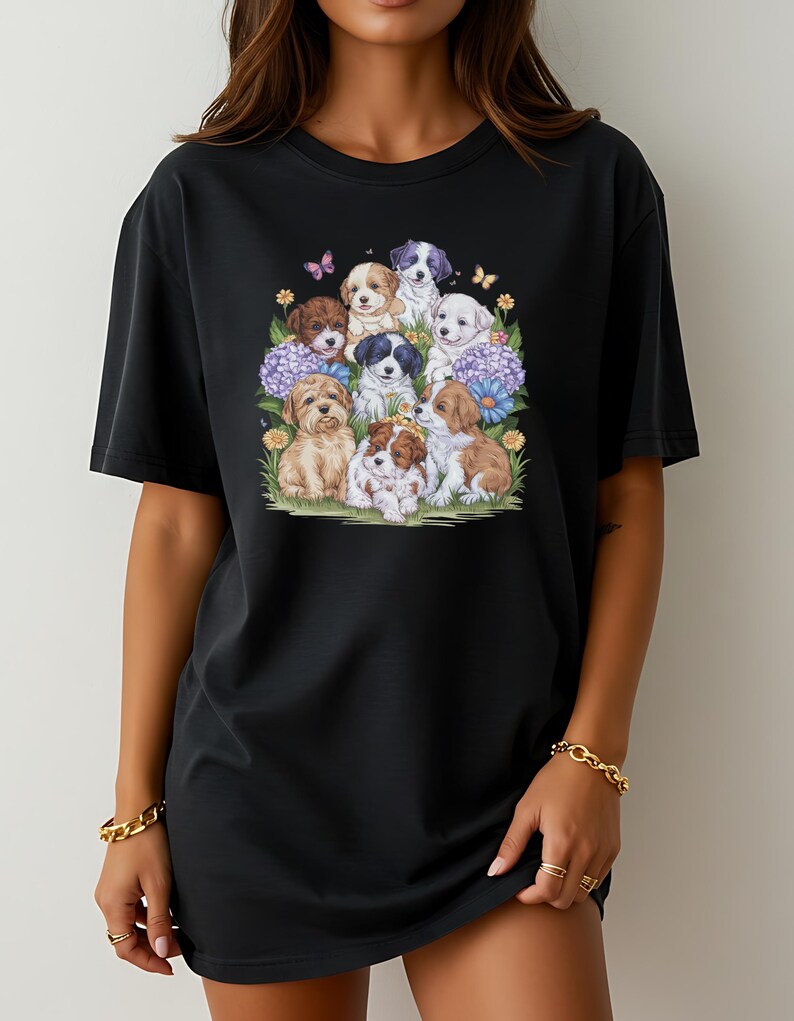 K&ouml;nnte beinhalten: Schwarzes Oversize-T-Shirt mit einem grafischen Druck einer Gruppe von Welpen, umgeben von Blumen und Schmetterlingen.