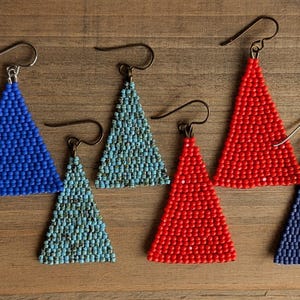 May include: Six pairs of triangle-shaped beaded earrings in blue, red, and turquoise. The earrings are made with small beads and have a simple, elegant design.