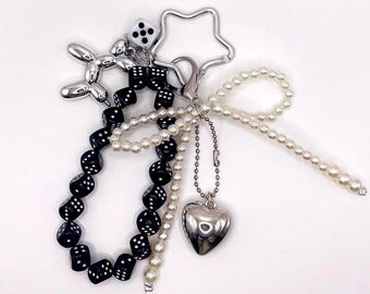 May include: A silver star-shaped keychain with a black and white dice charm, a silver balloon dog charm, a silver heart charm, and a string of black dice charms and white pearls.