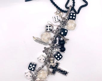 May include: A black and white charm bracelet with various charms, including dice, an Eiffel Tower, a cross, and an eight ball. The bracelet has a black star-shaped clasp and a black rubber band.