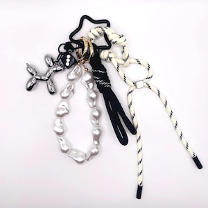 Może przedstawiać: Brelok do kluczy w kształcie srebrnego psa z balonu z naszyjnikiem z pereł, czarno-białym sznurkiem i czarnym brelokiem w kształcie gwiazdy.