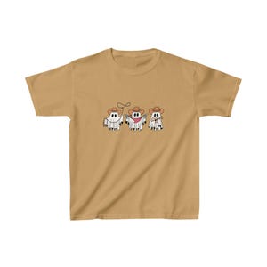 May include: Mustard-colored t-shirt featuring three cartoon ghosts dressed as cowboys. Each ghost wears a cowboy hat and has a different accessory: a lasso, a gun, and a sheriff's badge. The design is in black and white.