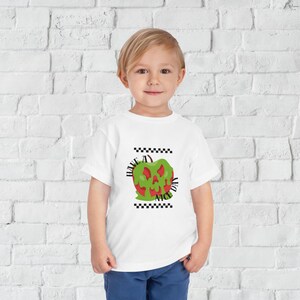 May include: White t-shirt with a green and red apple graphic. The apple has a scary face and the text "Have a Nice Day" is written around it.
