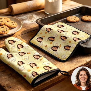 May include: A yellow oven mitt and pot holder set with a repeating pattern of a smiling face, chef hats, rolling pins, and cupcakes. Chocolate chip cookies are on a plate, and a baking sheet with cookies is nearby.