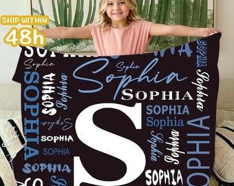 May include: A black blanket with the name "Sophia" in white and blue script. A large white "S" is centered on the blanket. The blanket is held by a person.