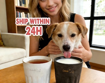 May include: Two ceramic mugs, one white and one dark gray, sit on a wooden surface. The white mug contains tea and has the name "Isaiah" and a dog silhouette. The dark gray mug has milk and the name "Lenoir" with a dog silhouette.