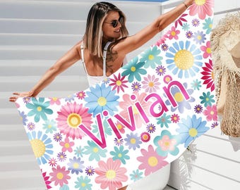 May include: A white beach towel with a vibrant floral pattern in pink, blue, yellow, and green. The name "Vivian" is printed in large pink letters across the towel. The towel is being held up against a white background.