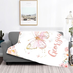 May include: A white throw blanket featuring a large pink and gold butterfly design with the name "Georgia" in pink script. The blanket is decorated with floral accents and small butterflies.