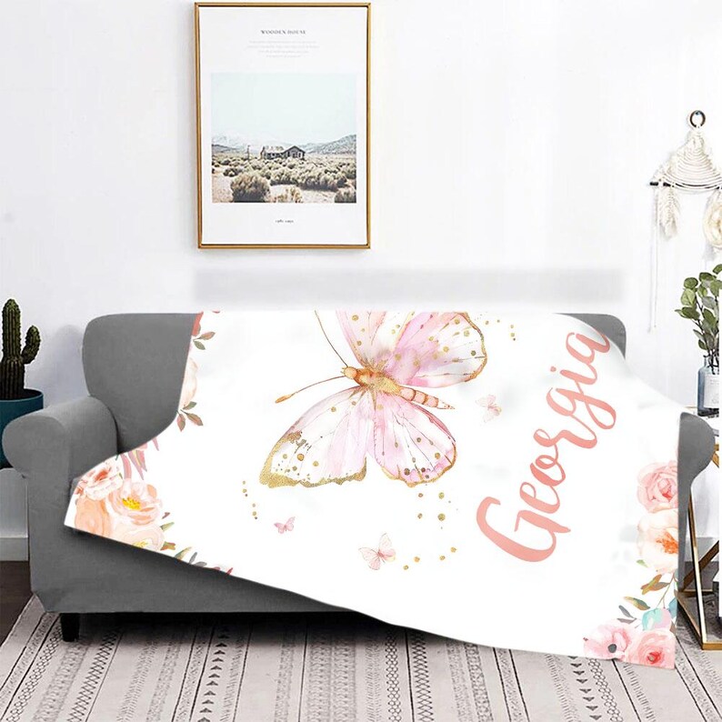 May include: A white throw blanket featuring a large pink and gold butterfly design with the name "Georgia" in pink script. The blanket is decorated with floral accents and small butterflies.