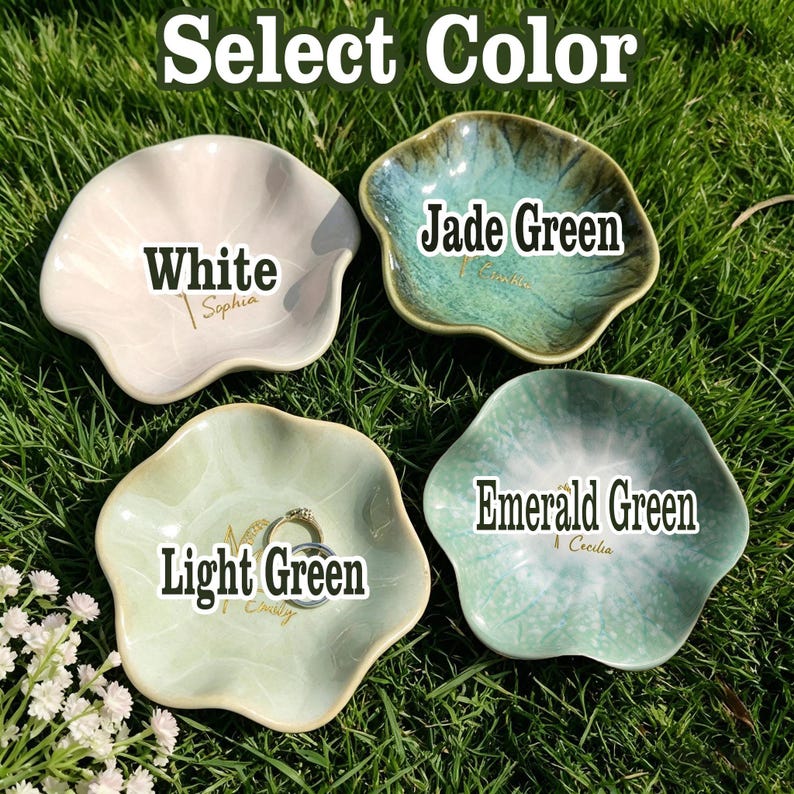May include: Four flower-shaped ceramic trinket dishes in white, jade green, light green, and emerald green. Each dish features a custom name printed in gold script. The white dish is labeled White, jade green as Jade Green, light green as Light Green, and emerald green as Emerald Green. A silver ring rests inside the light green dish.