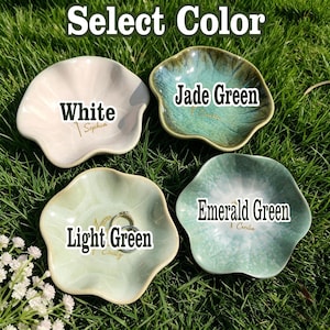 May include: Four flower-shaped ceramic trinket dishes in white, jade green, light green, and emerald green. Each dish features a gold-colored name inscription. The light green dish contains two silver-toned rings. The text Select Color is visible.
