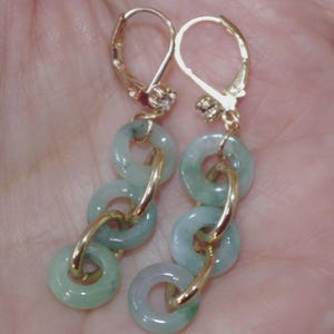May include: A pair of gold-toned earrings featuring a series of light green jade rings connected by gold links. The earrings have a lever back closure and small decorative accents near the top.