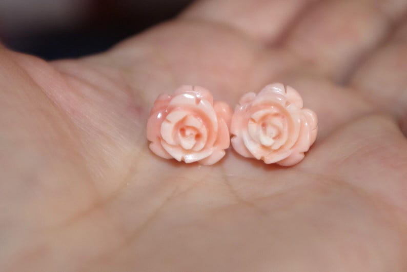 Puede incluir: Dos delicados pendientes en forma de rosa rosa claro. Los pendientes est&aacute;n tallados con detalles intrincados, mostrando los p&eacute;talos de las rosas. Los pendientes est&aacute;n colocados sobre un fondo borroso, resaltando el dise&ntilde;o de la joya. Estos pendientes son un hermoso accesorio.
