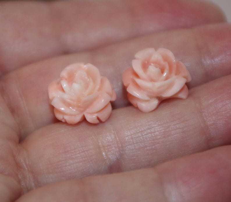 Puede incluir: Dos peque&ntilde;os objetos tallados en forma de rosa, de color melocot&oacute;n claro. Las tallas detalladas muestran los p&eacute;talos de las rosas. Los objetos se sostienen en una mano, lo que sugiere su peque&ntilde;o tama&ntilde;o. Las rosas parecen estar hechas de piedra u otro material duro.