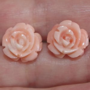 Puede incluir: Dos pendientes en forma de rosa rosa claro. Cada pendiente presenta p&eacute;talos detallados y un centro ligeramente m&aacute;s oscuro. Los pendientes son peque&ntilde;os y delicados, perfectos para a&ntilde;adir un toque floral a cualquier atuendo.