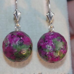 May include: A pair of earrings with large, spherical beads in shades of magenta and green. The earrings have gold-coloured lever-back ear wires. The beads have a marbled effect, with the magenta colour being the most prominent.