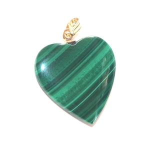 Puede incluir: Colgante en forma de corazón de malaquita verde con rayas verde oscuro. El colgante tiene una anilla dorada en la parte superior para sujetarlo a una cadena. La piedra está pulida y tiene un acabado brillante.