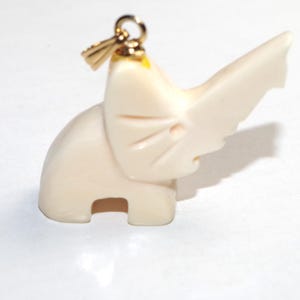 May include: Ivory-coloured elephant pendant with a gold-coloured bail. The elephant is carved with detailed features, including a raised trunk and etched lines. The pendant is a small, decorative accessory.