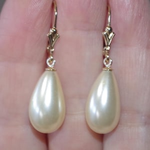 Puede incluir: Un par de pendientes colgantes con perlas de imitación en forma de lágrima, color crema. Los pendientes tienen cierres de palanca dorados. Las perlas tienen un brillo sutil. Diseñados para orejas perforadas.