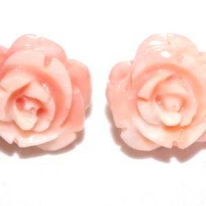Puede incluir: Dos adornos en forma de rosa de color melocot&oacute;n. Los p&eacute;talos est&aacute;n detallados con capas visibles, y el dise&ntilde;o general es suave y pulido. El fondo es blanco liso, resaltando las formas florales.