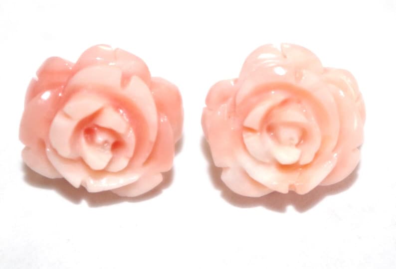 Puede incluir: Dos adornos en forma de rosa de color melocot&oacute;n. Los p&eacute;talos est&aacute;n detallados con capas visibles, y el dise&ntilde;o general es suave y pulido. El fondo es blanco liso, resaltando las formas florales.