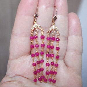 May include: Gold-toned dangle earrings featuring multiple strands of small, vibrant pink beads. The earrings have a decorative top with small, clear accents. The design is elegant and eye-catching, suitable for special occasions.