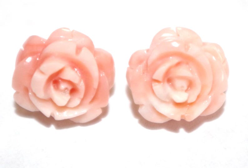 Puede incluir: Dos adornos en forma de rosa de color melocot&oacute;n. Los p&eacute;talos est&aacute;n detallados con capas visibles, y el dise&ntilde;o general es suave y pulido. El fondo es blanco liso, resaltando las formas florales.