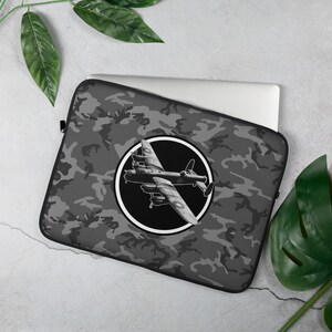 Pode incluir: Uma capa para laptop cinza com padrão de camuflagem. Uma silhueta preta e branca de um bombardeiro está centrada na capa.