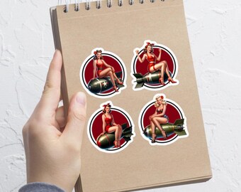 Könnte beinhalten: Vier runde Aufkleber mit Pin-up-Illustrationen von Frauen in roten Kleidern, die auf Bomben mit rot-weiß-blauen Akzenten sitzen.