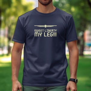 Puede incluir: Una camiseta azul marino con un diseño gráfico blanco. El gráfico presenta un avión estilizado con el texto "Sweet Liberty My Leg!!"
