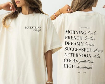 May include: A white oversized t-shirt with the text "EQUESTRIAN Lifestyle" on the front and "EQUESTRIAN MORNING hacks FRENCH leather DREAMY horses SUCCESSFUL shows AFTERNOON rides GOOD equitation HIGH standards LIFESTYLE" on the back.