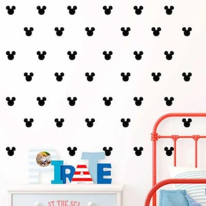 May include: Black Mickey Mouse head wall decals are scattered across a white wall. A red metal bed frame is visible on the right. A white dresser with blue and red letters spelling "PIRATE" is in the foreground.