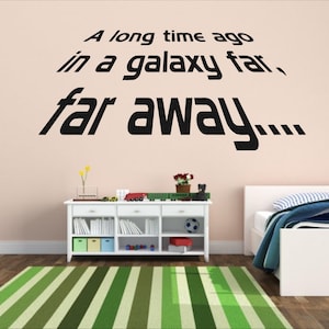 May include: A white wall with black text that reads "A long time ago in a galaxy far, far away..." The text is in a stylized font. There is a white bookshelf with a green rug in front of it. A white bed with a blue and white patterned bedspread is in the background.