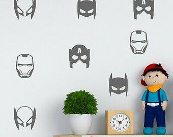 May include: A set of superhero masks wall decals in dark gray. The masks include Batman, Iron Man, Captain America, and Wolverine. The decals are shown on a white wall with a clock and a potted plant.
